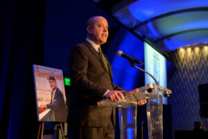 Chris Carr introducing Pat Wilson on the stage at a podium at the Georgia Aquarium Ocean's Ballrom