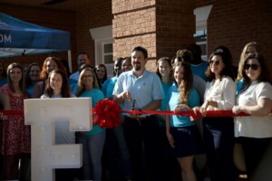 Ribbon cutting with a group of poeple and red ribbon and big scissors