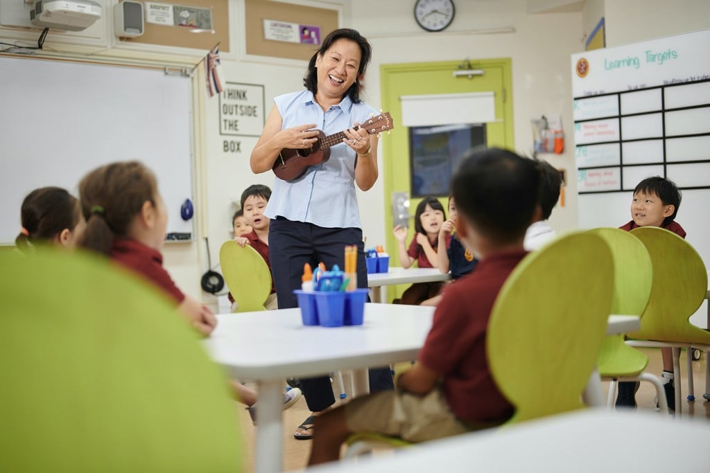 A teacher playing ukelele for elementary students at Maryknoll school