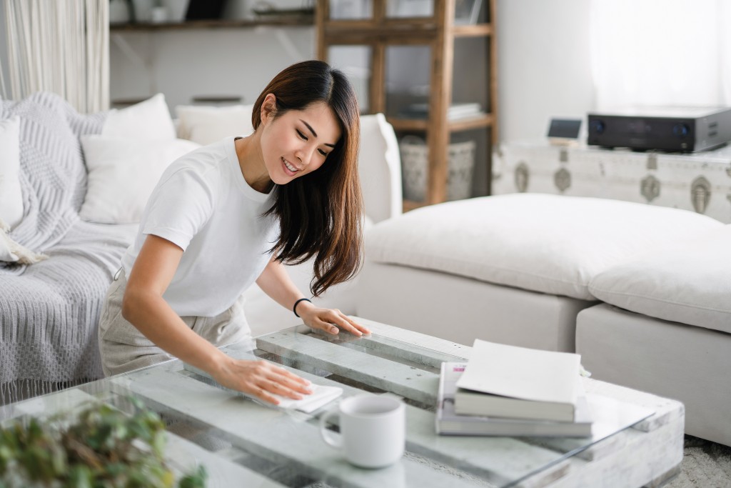 Young Woman Tidying Up The Living Room And Wiping The Coffee Table Surface With A Cloth