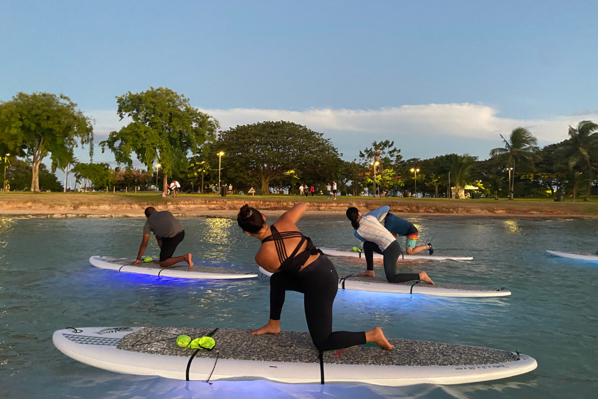 Woman practice yoga asana on paddle board at night