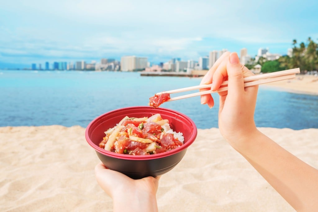 A Girl Eating And Enjoying Hawaiian Ahi Poke Bowl On Waikiki Beach