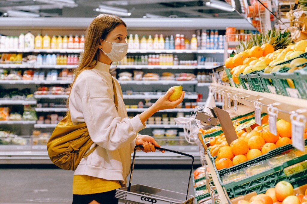 woman in mask in grocery store holding a lemon (Source: Pexels/Anna Shvets)