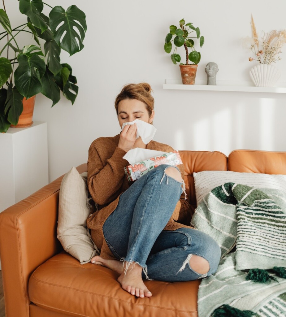 woman on couch blowing nose in a tissue (Source: Pexels/Karolina Grabowska)