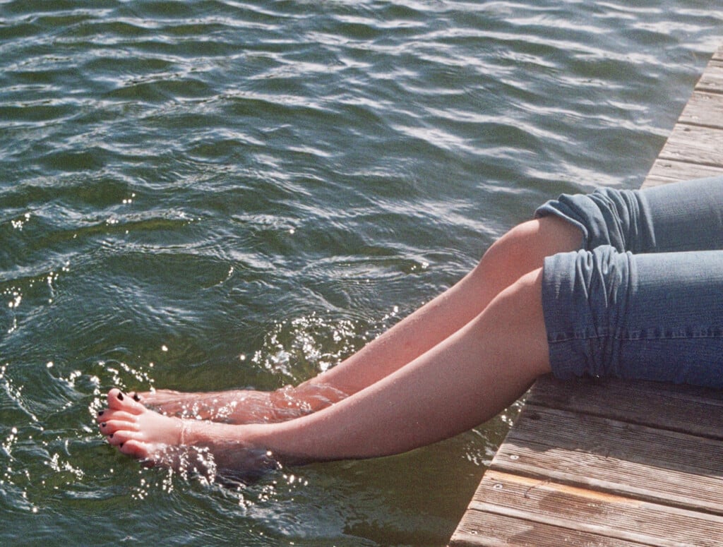 person sitting on dock with legs in lake water (Source: Pexels/Bruno Silva)