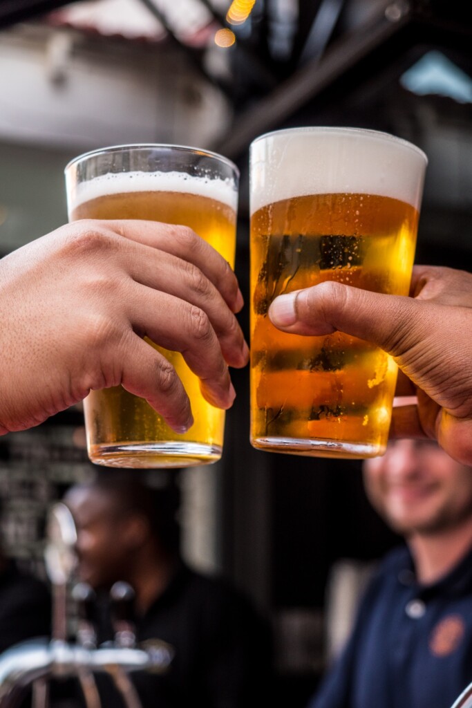 two hands hold glasses of beer (Source: Pexels/Tembela Bohle)