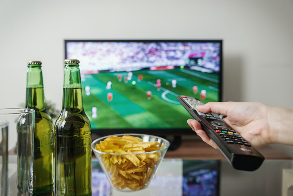 TV remote, bowl of chips, hand holding remote pointed at TV (Source: Pexels/JESHOOTS.com)