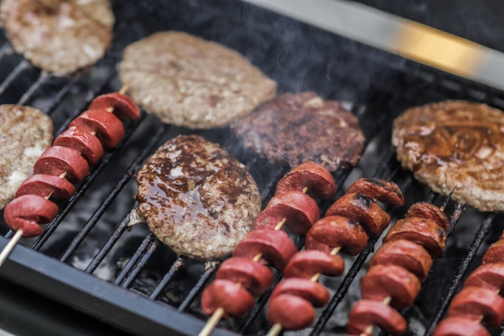 hamburgers and spiral hot dogs on a grill (Source: Pexels/Luis Quintero)