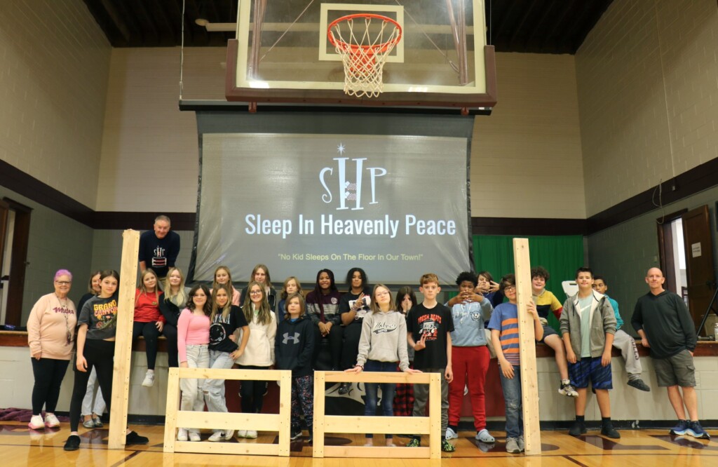 The PBJHS community service class, under the instruction of Allison Bell, poses with headboards and side rails of a bed built for a child in need alongside the Elledges, and build director Steve Keith. (Source: Poplar Bluff R-I School District)