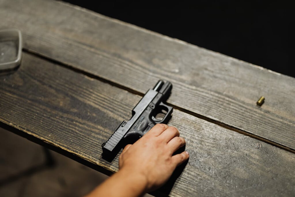 gun and hand on table (Source: Pexels/Karolina Kaboompics)