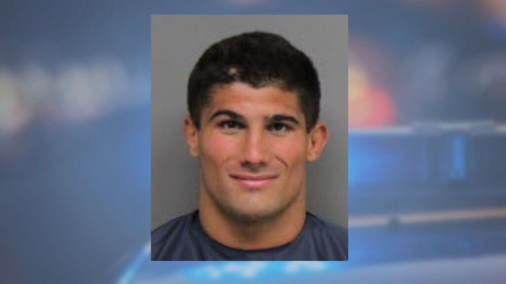 AJ ferrari mugshot with police lights behind him.