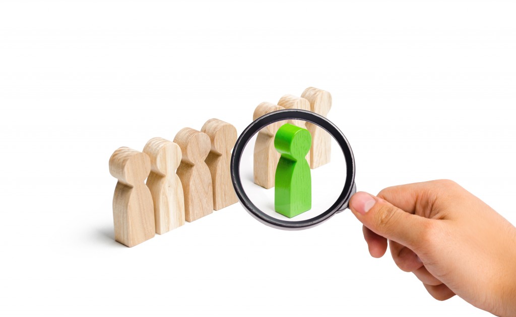 Magnifying Glass Is Looking At The Green Figure Of A Man Comes Out Of The Line Of People. Concept Of Success And Improvement In Work, The Universal Recognition Of Efficiency And Leadership Qualities.