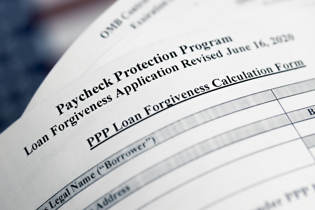 Selective Focus Photo Of Paycheck Protection Program Loan Forgiveness Application Form Revised, On A Background Of United States Flag. Paycheck Protection Program New Round.