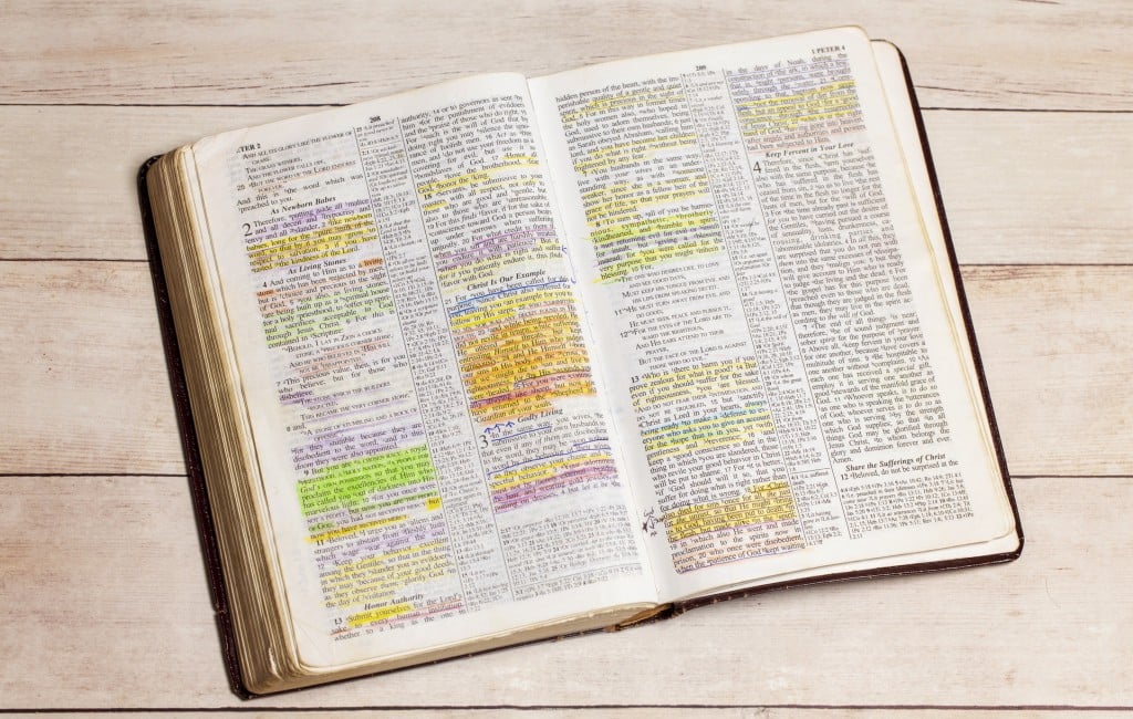 A Used And Highlighted Bible Open On A White Wood Table