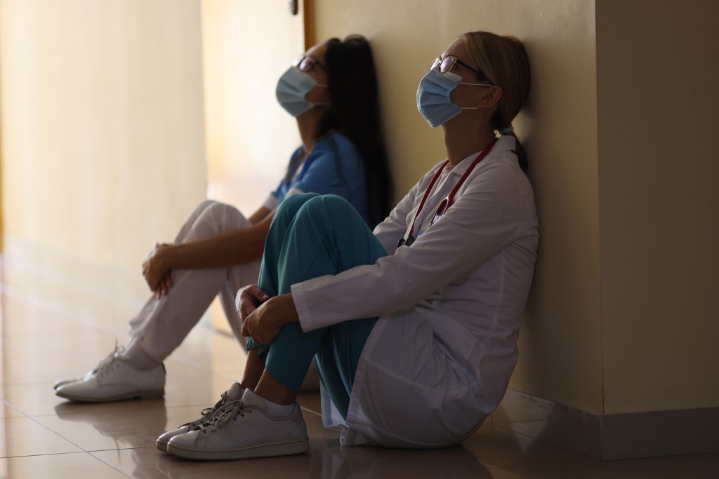 Young Female Doctor And Nurse In Medical Masks Sit In Corridor Of Hospital