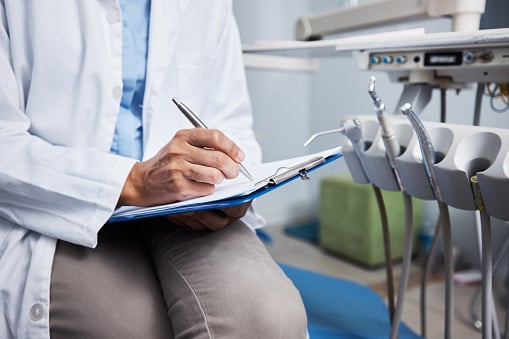 Shot Of An Unrecognisable Dentist Writing Notes On A Piece Of Paper