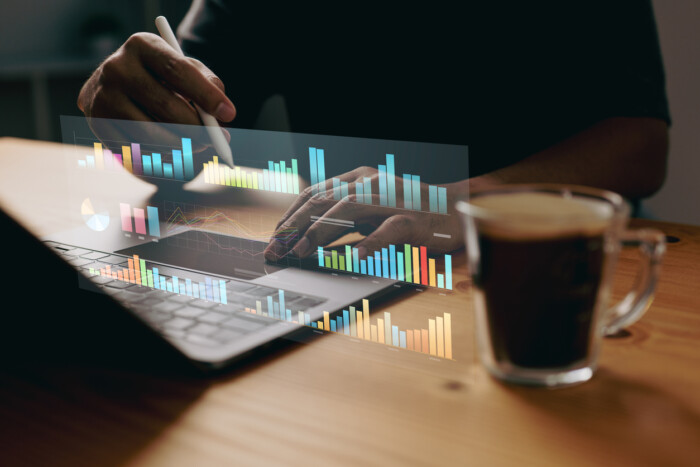 digital graph overlaid a person typing on laptop with cup of coffee next to them on desk