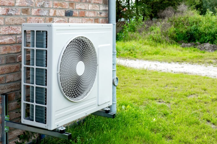 Heat Pump, Sustainable Heating Solution For Modern Homes. Environmentally Friendly Heat Pump Technology In Front Of A Brick House.