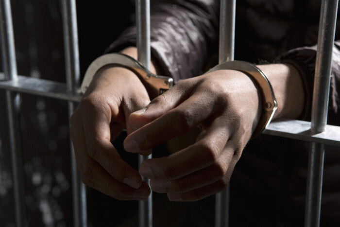 A Prisoner Behind Bars With Hands Cuffed