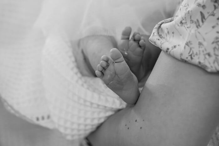 Newborn Baby Feet Close Up On Mother's Lap: Black And White Photo Showing First Tender Moments, Soft Texture, Skin Tone, Parenthood, And Love.