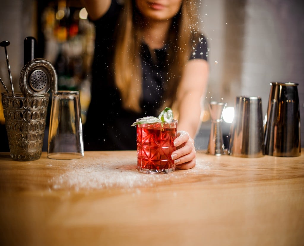 Barista Finishes Preparation Of R Cocktail With Mint Leaves By Adding A Bitter Of Powdered Sugar