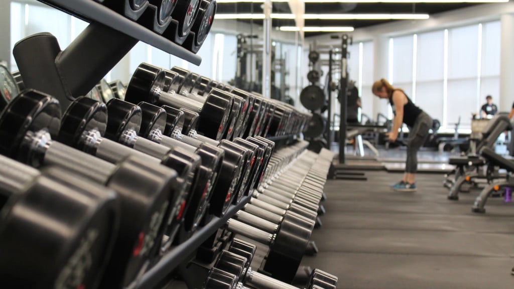 A woman works out by a rack of dumbbells.