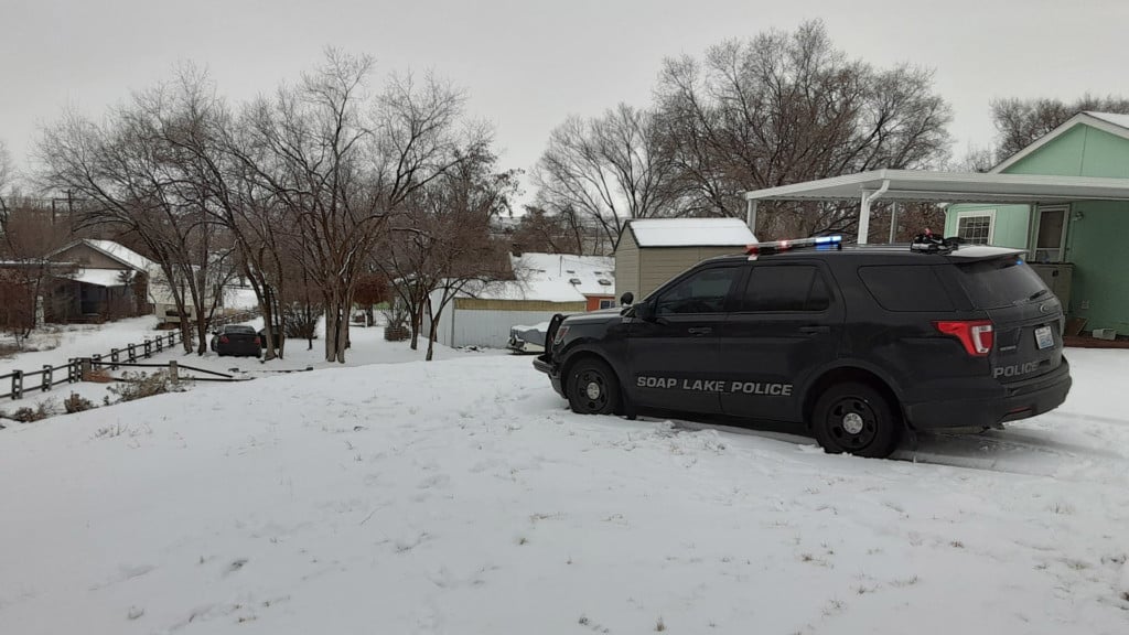 Soap Lake Police patrol car parked in front of a house, with a suspect vehicle abandoned in the backyard.