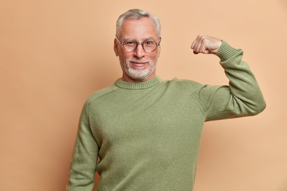 Confident,satisfied,grey,haired,man,raises,arm,and,shows,muscle