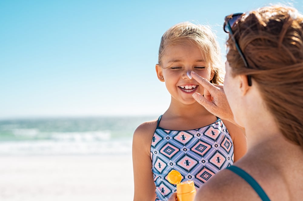 Young,mother,applying,protective,sunscreen,on,daughter,nose,at,beach.