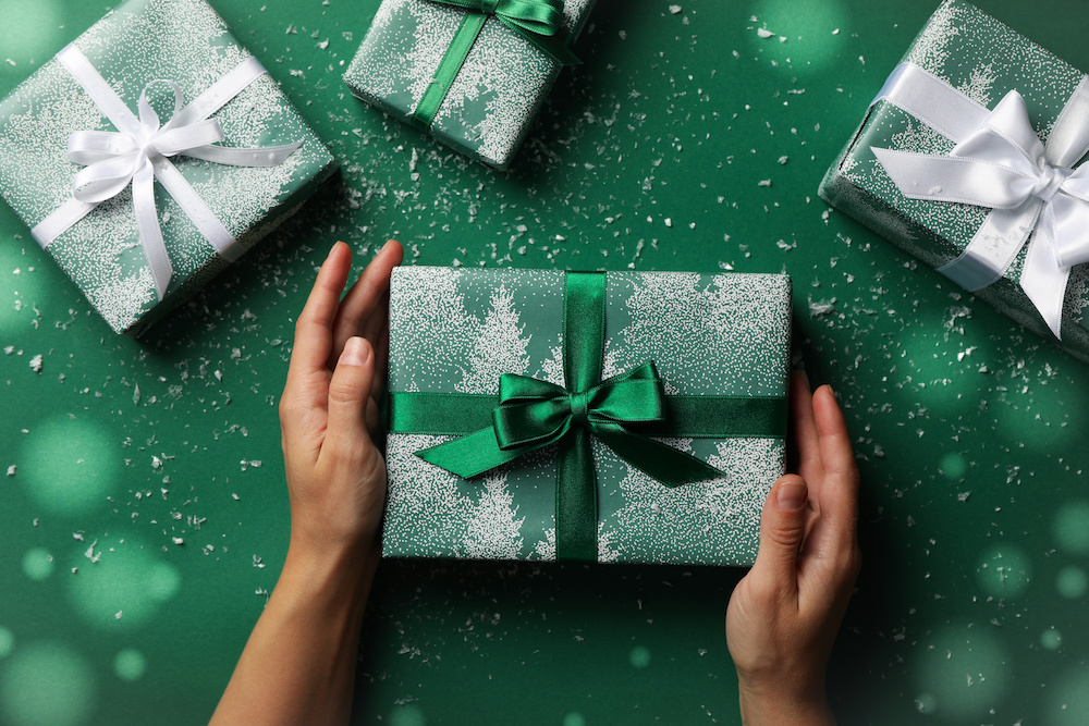 Female Hands Hold Gift Box On Green Background