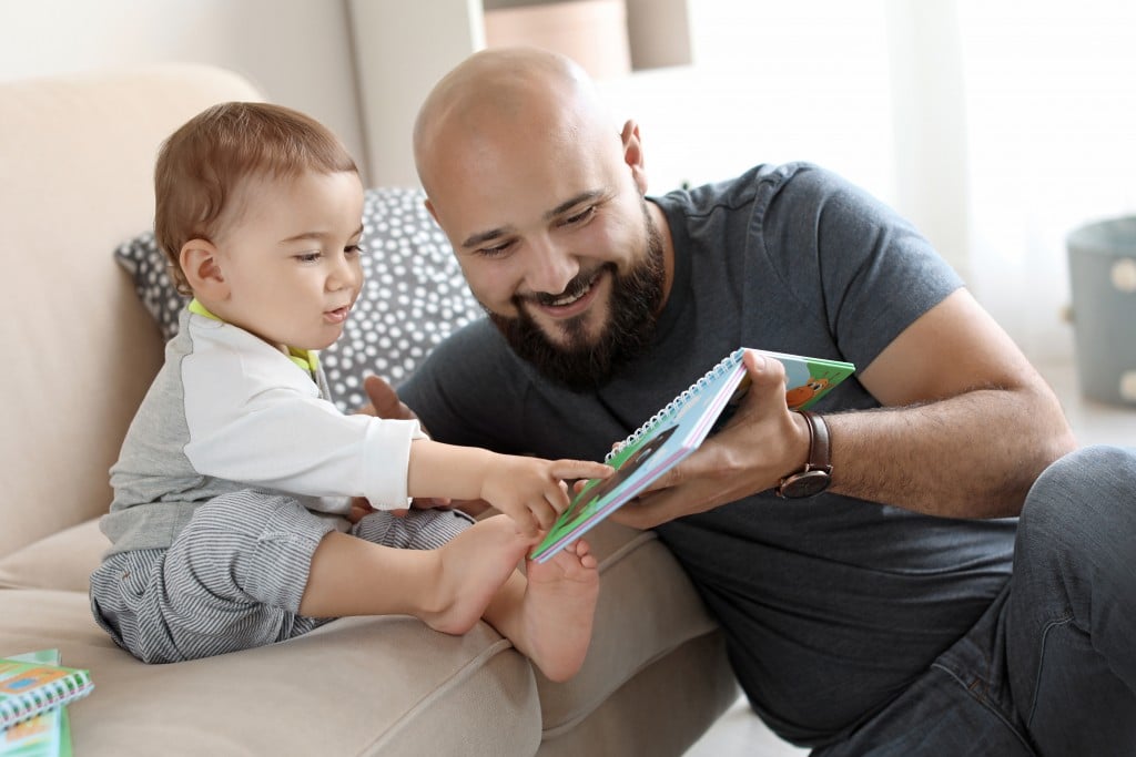Dad Reading Book With His Little Son In Living Room