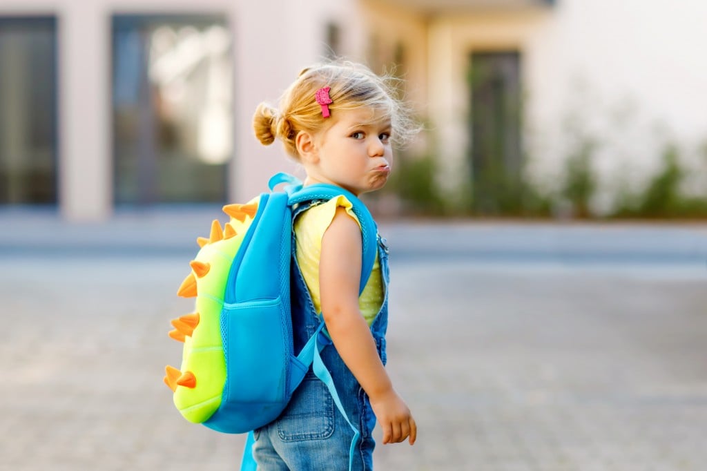 Cute Little Adorable Toddler Girl On Her First Day Going To Playschool. Healthy Upset Sad Baby Walking To Nursery School. Fear Of Kindergarten. Unhappy Child With Backpack On The City Street, Outdoors