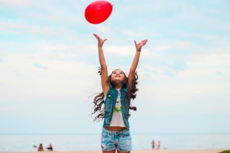 A girl in a denim vest throwing a red balloon.