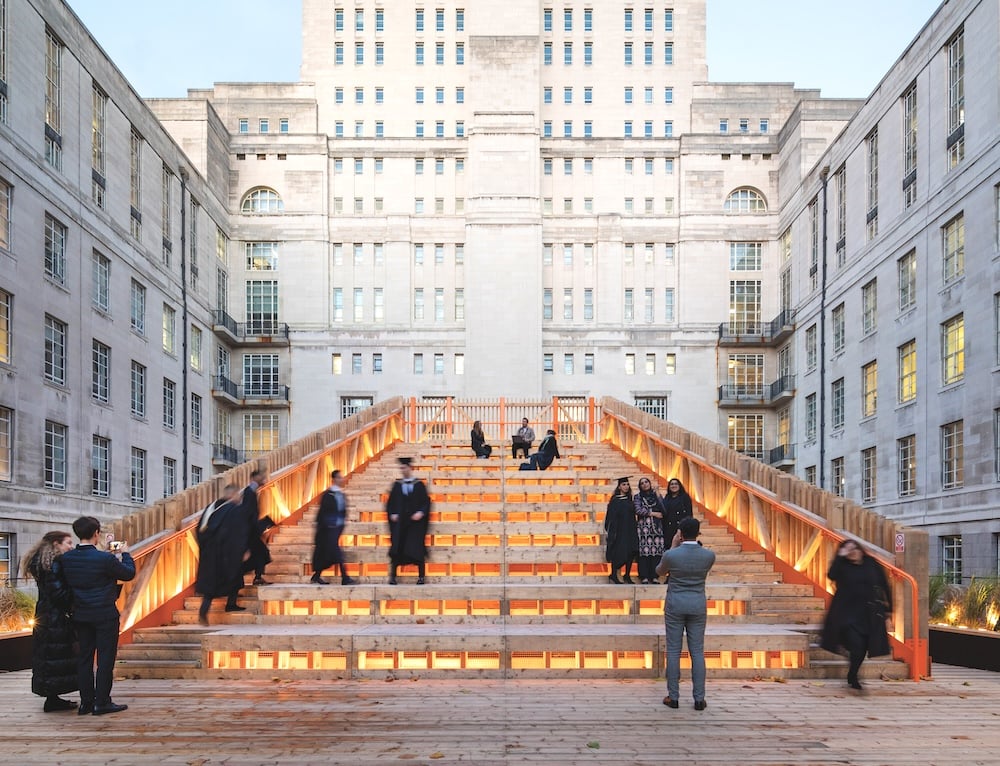 A set of wooden stairs in a courtyard at the University of London, with students relaxing on them