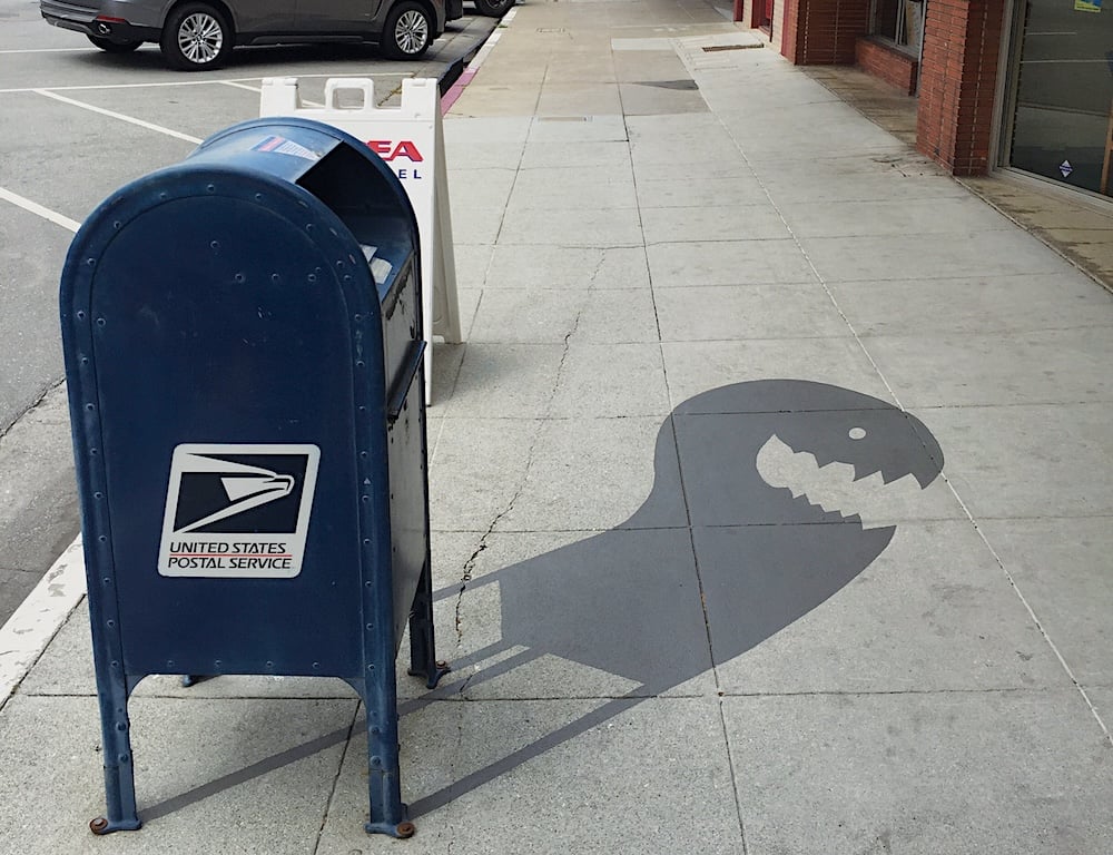A piece of shadow art that gives a mailbox the fake shadow of a creature with an open mouth