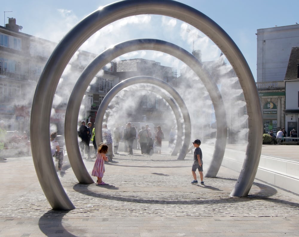 An example of public art misters in the form of large vertical rings with children running through them.