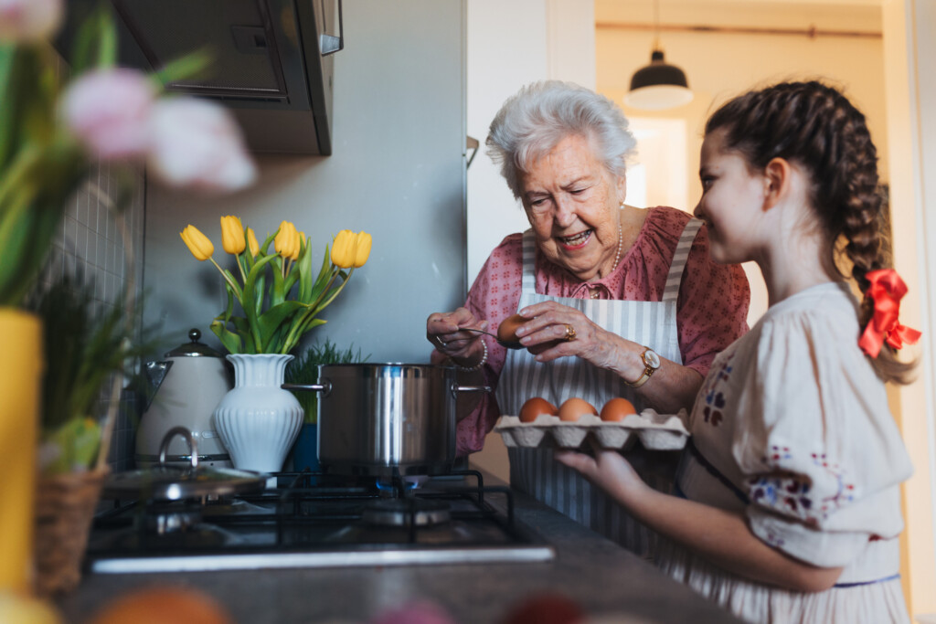 Grandmother With Granddaughter Preparing Traditional Easter Meals, Boiling Eggs With Natural Dye To Colour Shells. Passing Down Family Recipes, Custom And Stories.