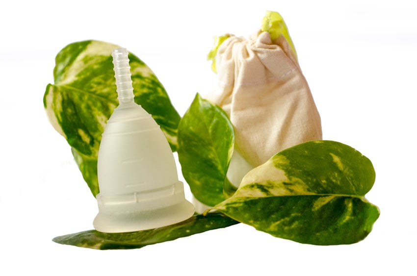 White Menstrual Cup With Green Leaves And Little Beige Bag Isolated In White Background.