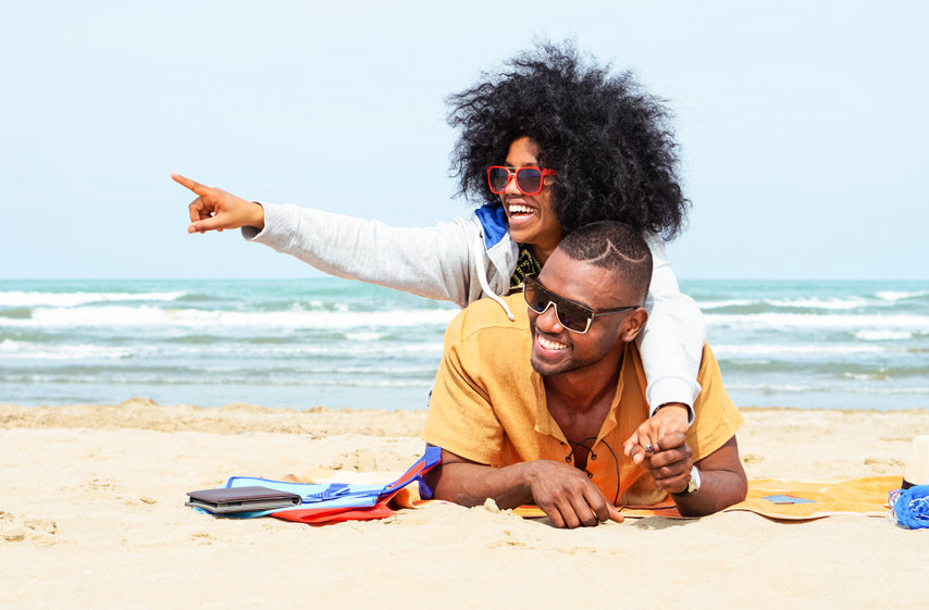 Young Afro American Couple Pointing Finger Relaxing On Beach 
