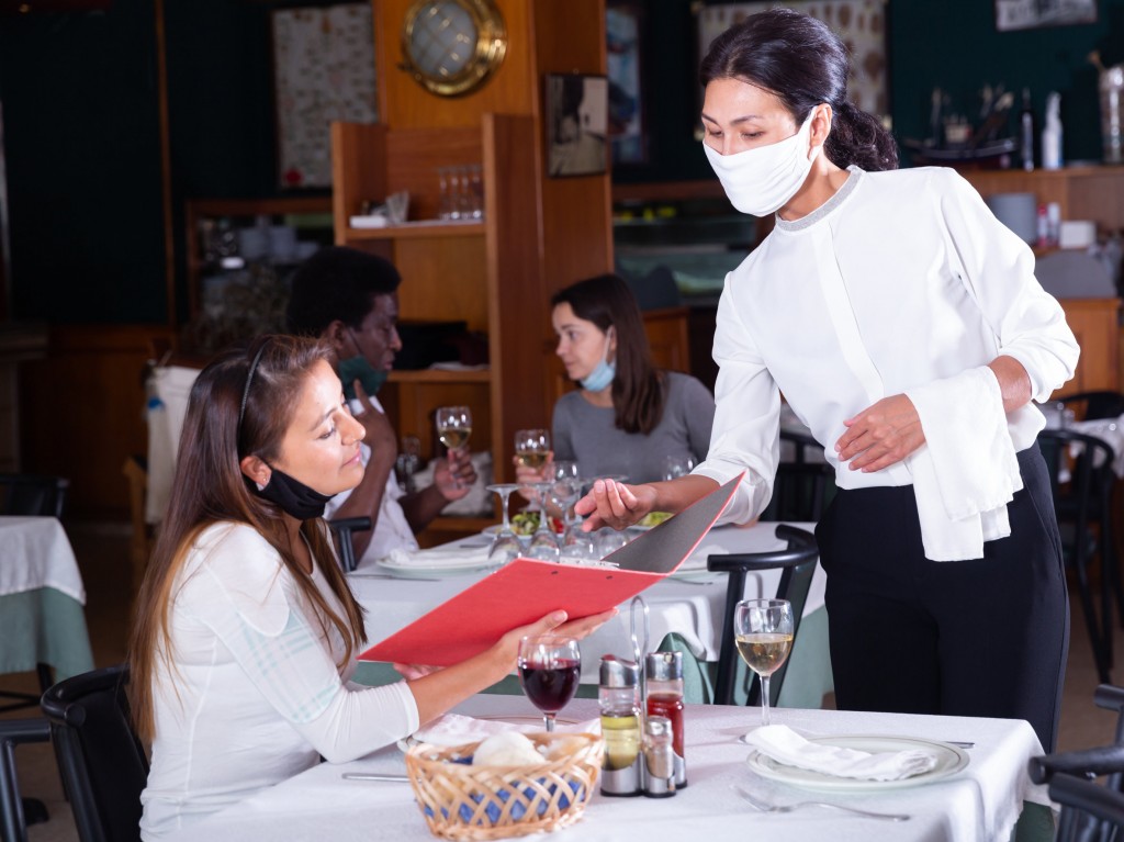 Smiling Female Waiter Taking Order From Woman In Restaurante Diring Virus