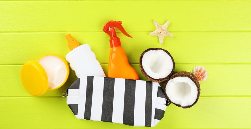 Sunscreen Bottles With Seashells, Coconuts And Case On Green Wooden Table