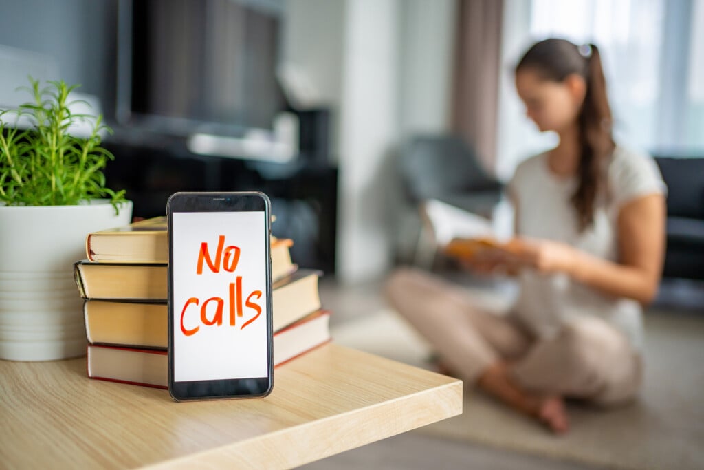 Digital Detox Concept Photo. Smartphone With The Text No Calls And Woman Reading Book In The Background