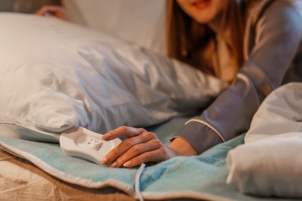 Young Woman Lying On Electric Heating Pad In Bedroom At Night, Closeup