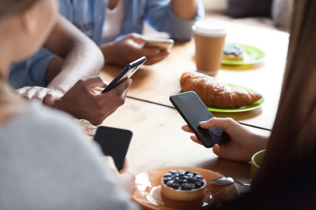 Close Up Multiracial People Sitting In Cafe Together, Using Phones