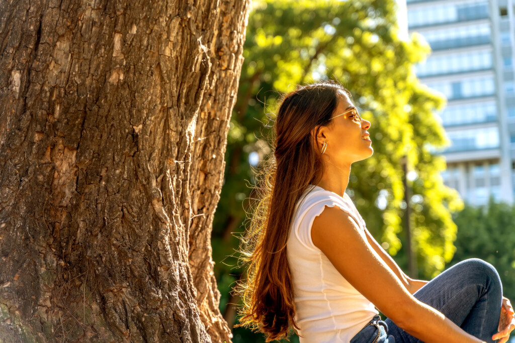 A Young Woman Sitting Next To A Tree And Enjoying The Sunshine