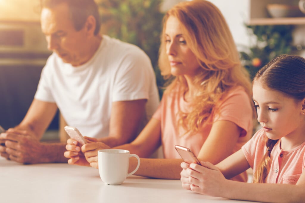 Three Members Family Absorbed In Smartphones During Breakfast