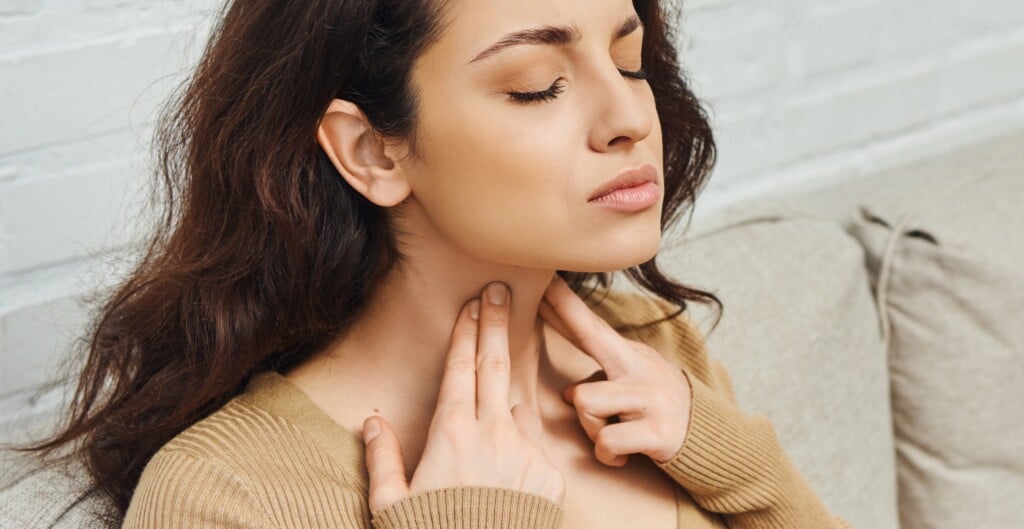 Young Woman In Casual Jumper Massaging Lymphatic Nodes On Neck During Wellness Routine On Couch At Home, Self Care Ritual And Holistic Wellness Practices Concept, Banner, Tension Relief