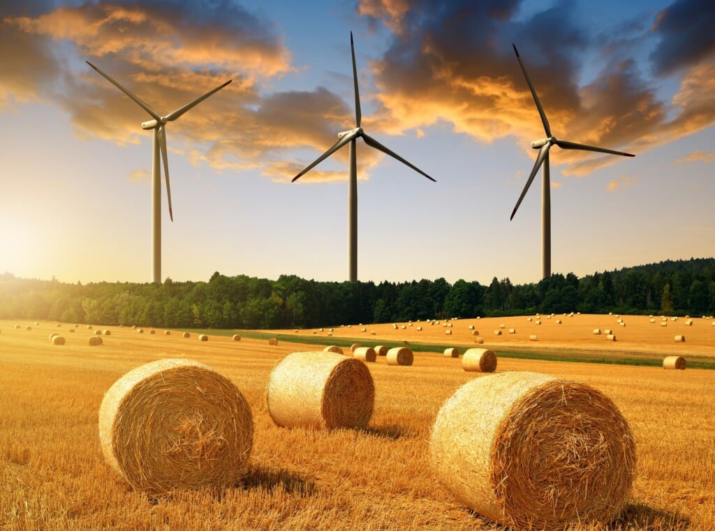 Straw Bales On Farmland And Wind Turbines At Sunset