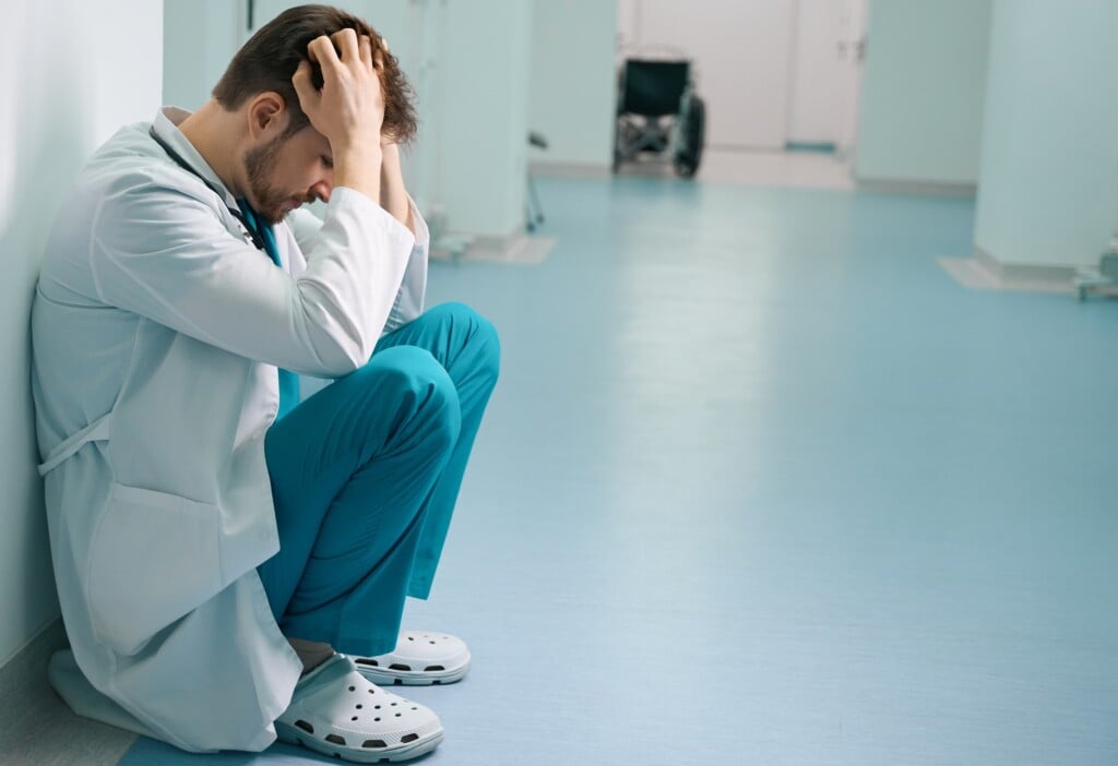 Upset Young Intern Squatting In Hospital Corridor
