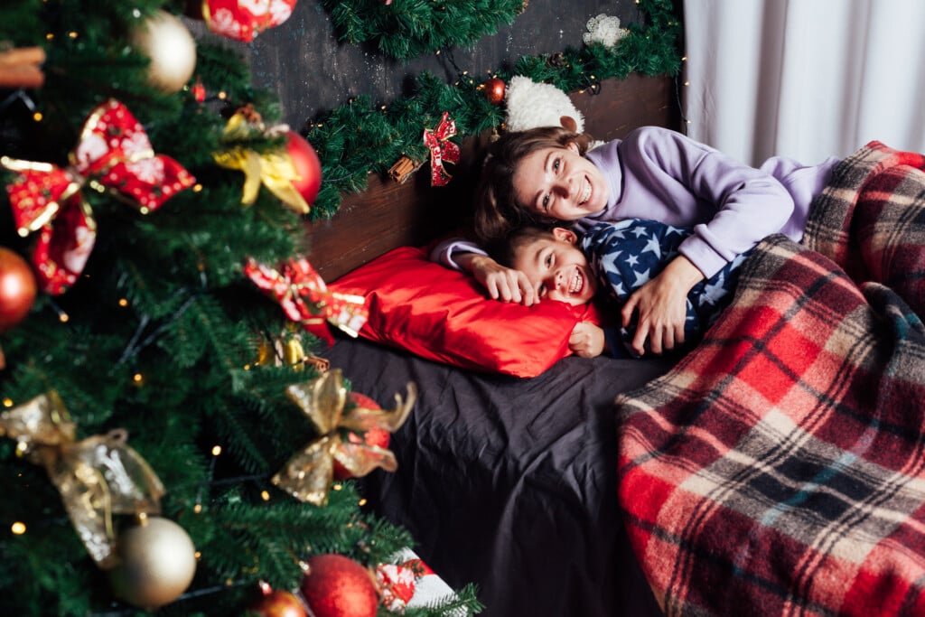 Mom And Son Lie In The Bed By The Christmas Tree With Gift Lights Garland New Year
